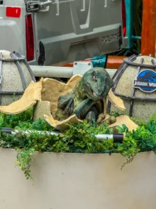 Un bébé dinosaure animatronique sortant de son œuf cassé dans un nid de verdure, lors de l'animation Jurassic World à Universal Studios Singapore.