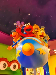 Personnages de Sesame Street dont Elmo, Ernie, Bart et Big Bird à bord d'une navette spatiale colorée dans le décor de l'attraction Spaghetti Space Chase à Universal Studios Singapore.