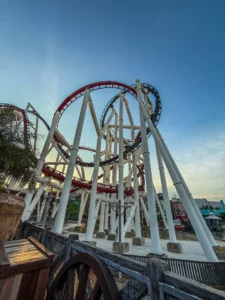 Vue en contre-plongée des montagnes russes Battlestar Galactica: Human vs. Cylon à Universal Studios Singapore, montrant les rails rouges et gris entrelacés sur des supports blancs sous un ciel clair au coucher du soleil.
