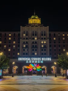 Vue nocturne de l'imposante entrée d'Universal Studios Beijing, illuminée par le logo coloré du parc et le nom de l'établissement en lettres lumineuses sur le bâtiment principal.
