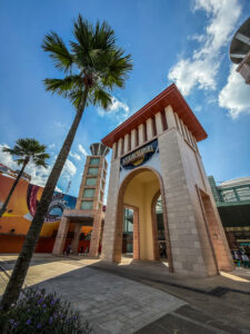 Photographie de l'arche d'entrée monumentale en pierre de Universal Studios Singapore avec des palmiers sous un ciel bleu nuageux.