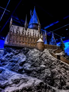 L'immense maquette détaillée du château de Poudlard recouverte d'un fin manteau de neige et perchée sur ses falaises rocheuses, illuminée sous des projecteurs bleus en intérieur.