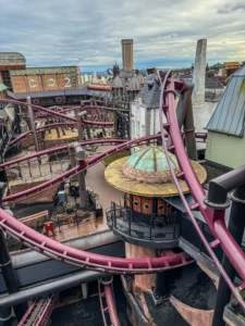 Vue aérienne de la zone immersive Rookburgh à Phantasialand, montrant les rails sinueux en métal bordeaux des montagnes russes F.L.Y. entrelacés au milieu de décors industriels de style steampunk.