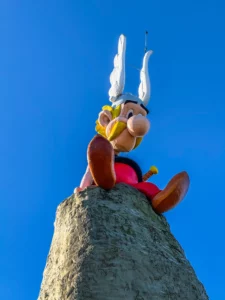 La célèbre statue géante du personnage gaulois Astérix assis au sommet de son rocher sous un ciel bleu azur à l'entrée du Parc Astérix.